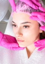 Close up of the beautiful face of a young woman. Many hands holding cosmetology tools near face of a patient