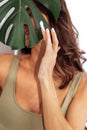 Close up of beautiful female brunette hides her face behind monstera leaf. Young smiling caucasian woman smears green leaf with Royalty Free Stock Photo