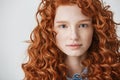 Close up of beautiful girl with curly red hair and freckles looking at camera over white background. Royalty Free Stock Photo