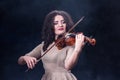 Close-up. Beautiful girl with dark hair on a smoky background. Violin and bow in female musical hands. Beautiful girl