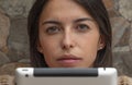 Close-up of beautiful girl sitting with the tablet. Adolescence holding a notebook hiding after the screen. Serious Teenager