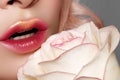 Close-up of beautiful lips with bright kissed makeup and gold glitter. Fashion red tint visage with white rose flower Royalty Free Stock Photo