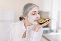 Close up of beautiful senior gray haired lady with white clay cosmetic mask on her face, enjoying spa time at home and Royalty Free Stock Photo