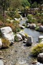 Close up of a beautiful, shallow stream running over rocks in a garden setting with a wooden bridge a stream