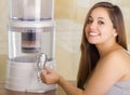 Close up of a beautiful smiling woman filling a glass of water, with a filter system of water purifier on a kitchen