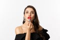 Close-up of beautiful woman applying red lipstick on lips, looking at camera like mirror, standing in black dress over Royalty Free Stock Photo