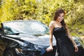 Close up of beautiful woman wearing a black dress and a red flower in her head and posing in front of a luxury black car Royalty Free Stock Photo