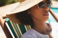 African American woman with hat and sunglasses relaxing on sun lounger in her backyard Royalty Free Stock Photo