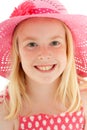 Close up of beautiful young blonde girl with a big smile wearing a big pink floppy hat and looking directly at the camera. Royalty Free Stock Photo