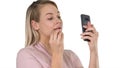 Beautiful young blonde woman which is painting her lips with red lipstick and looking in the phone on white background. Royalty Free Stock Photo