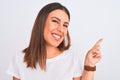 Close up of beautiful and young brunette woman standing over isolated white background very happy pointing with hand and finger to Royalty Free Stock Photo