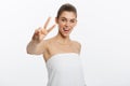 Close-up of beautiful young woman with bath towel covering her breasts, on gray, shows two fingers sign Royalty Free Stock Photo