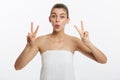 Close-up of beautiful young woman with bath towel covering her breasts, on gray, shows two fingers sign Royalty Free Stock Photo