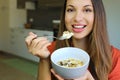 Close up of beautiful young woman eating skyr yogurt with cereal muesli fruit at home, looking at camera, focus on the model eyes Royalty Free Stock Photo