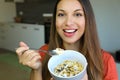 Close up of beautiful young woman eating skyr yogurt with cereal muesli fruit at home, looking at camera, focus on the model eyes Royalty Free Stock Photo