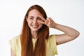 Close up of beautiful young woman with natural pale skin and freckles, red long hair, show peace v-sign and smiling Royalty Free Stock Photo