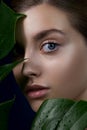 Close-up of beautiful young woman`s face with perfect skin through the tropical green leaves Royalty Free Stock Photo