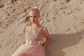 Close-up portrait of a blonde woman posing in embroidery dress in the desert, lying on golden sand with closed eyes. Royalty Free Stock Photo