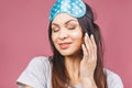 Close up beauty portrait of a laughing beautiful woman in sleeping mask applying face cream and looking away isolated over pink Royalty Free Stock Photo