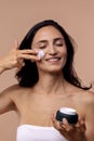 Close-up beauty studio portrait of an attractive young woman applying moisturizing cream to her face on a beige isolated Royalty Free Stock Photo
