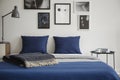 Close-up of bed with blue bedding and dark colored blanket. Bedside table with books and coffee next to it. Royalty Free Stock Photo