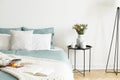 Close-up of a bed with pale sage green and white linen, pillows and a blanket in a sunny bedroom interior. A round black metal sid