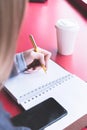 Close-up from behind the back of a young woman in a winter polto is holding a ballpoint pen and is going to write Royalty Free Stock Photo