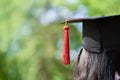 Close-up Behind photo of university graduate wears gown and black cap, red ribbon and green blur bokhe background Royalty Free Stock Photo