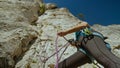CLOSE UP: Belayer creates slack in rope attached to climber scaling a cliff.