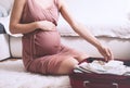 Close-up belly of pregnant woman with travel bag of clothes and necessities. Mother during pregnancy preparing and packing