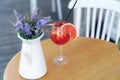 A close-up berry-citrus cocktail stands in a glass on a table next to a decorative vase of wildflowers. The interior