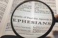 closeup of the epistle of Paul to the Ephesians from Bible using a magnifying glass to enlarge print.