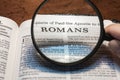 closeup of the epistle of Paul to the Romans from Bible using a magnifying glass to enlarge print.