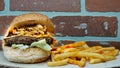 Big juicy hamburger with caramelized onions, cheddar cheese, french fries, lettuce on wooden tray with brick wall background Royalty Free Stock Photo