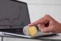 Close-up of Bitcoin and Ethereum cryptocurrencies held up by a finger with candlestick charts in the background of a laptop.