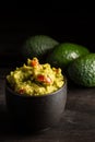 Close up of black bowl with guacamole on dark table with three avocados, selective focus, vertical