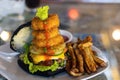 Close up of black bun cheese burger with fried onion rings on top, french fries and ketchup Royalty Free Stock Photo