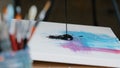 Close-up black dark paint splatters on canvas with pink and blue color picture female hand holding paint brush draws