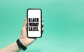 Close-up of black friday sales text on white screen on smartphone in male hand. Background of cyan, aqua menthe color.