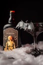 Close-up of black Halloween cocktail glass with bat, skeleton and bottle of poison on spider web, black background,