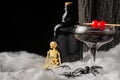 close-up of black Halloween cocktail glass with red cherries, skeletons, spiders and dark bottle on spider web, black background, Royalty Free Stock Photo