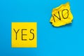 Close up black handwritten inscription yes and no word on two yellow square stickers on blue background with copy spase, Royalty Free Stock Photo