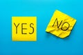 Close up black handwritten inscription yes and no word on two yellow square stickers on blue background with copy spase, Royalty Free Stock Photo