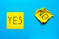 Close up black handwritten inscription yes and no word on two yellow square stickers on blue background with copy spase,