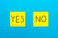 Close up black handwritten inscription yes and no word on two yellow square stickers on blue background with copy spase,