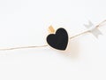 Close-up black heart wooden chalkboard clothespin on rope twine on white wall, vertical. Detail of garland Valentine day Royalty Free Stock Photo