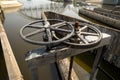 Close-up of black metal cogwheel controlling floodgate with texts in Thai language meaning `the property of` on one side.