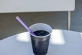 Close-up of black paper cup with purple straw and dark beverage, placed on white surface table Royalty Free Stock Photo