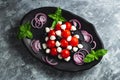 Close-up on a black plate with fresh caprese salad with basil, cherry tomatoes, mini mozzarella balls, topped with balsamic