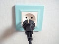 Close-up of a black plug near a blue outlet on the wall. The concept of the need for electricity. Electrical appliances, dangerous Royalty Free Stock Photo